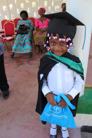 Criança com chápeu de graduação e vestida com traje escolar